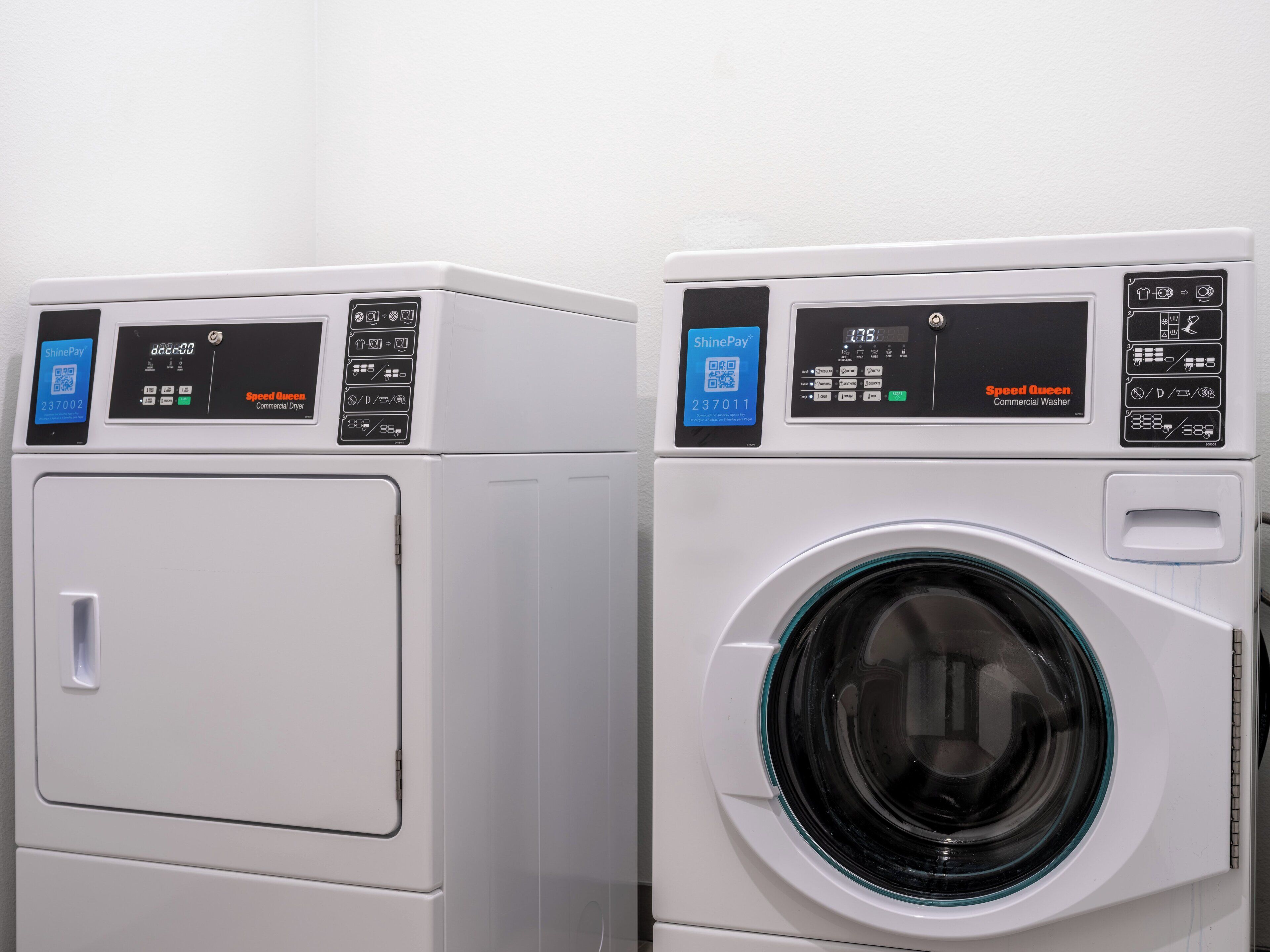 Twee witte commerciële wasmachines, waarvan één met een voorlader en de andere met een bovenlader, beide met digitale displays en bedieningspanelen.
