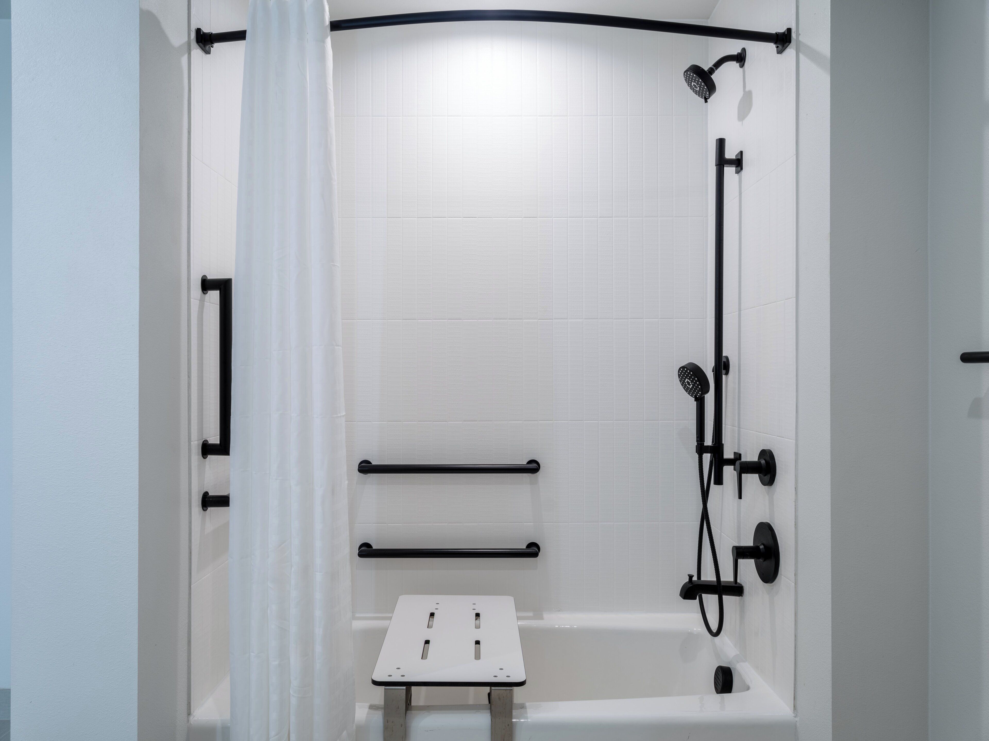 Un espace douche moderne avec un mur recouvert de carreaux blancs, des accessoires noirs et un petit banc.