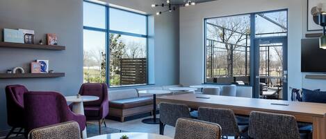 A modern dining area with a long table, multiple chairs, and a large window offering a view of the outdoors.