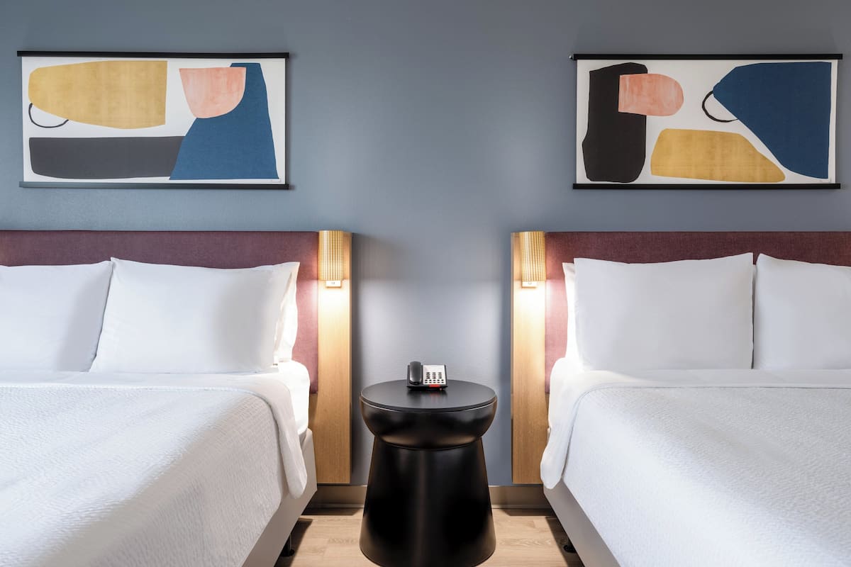 A hotel room with two beds, a small round table, and abstract artwork on the walls.