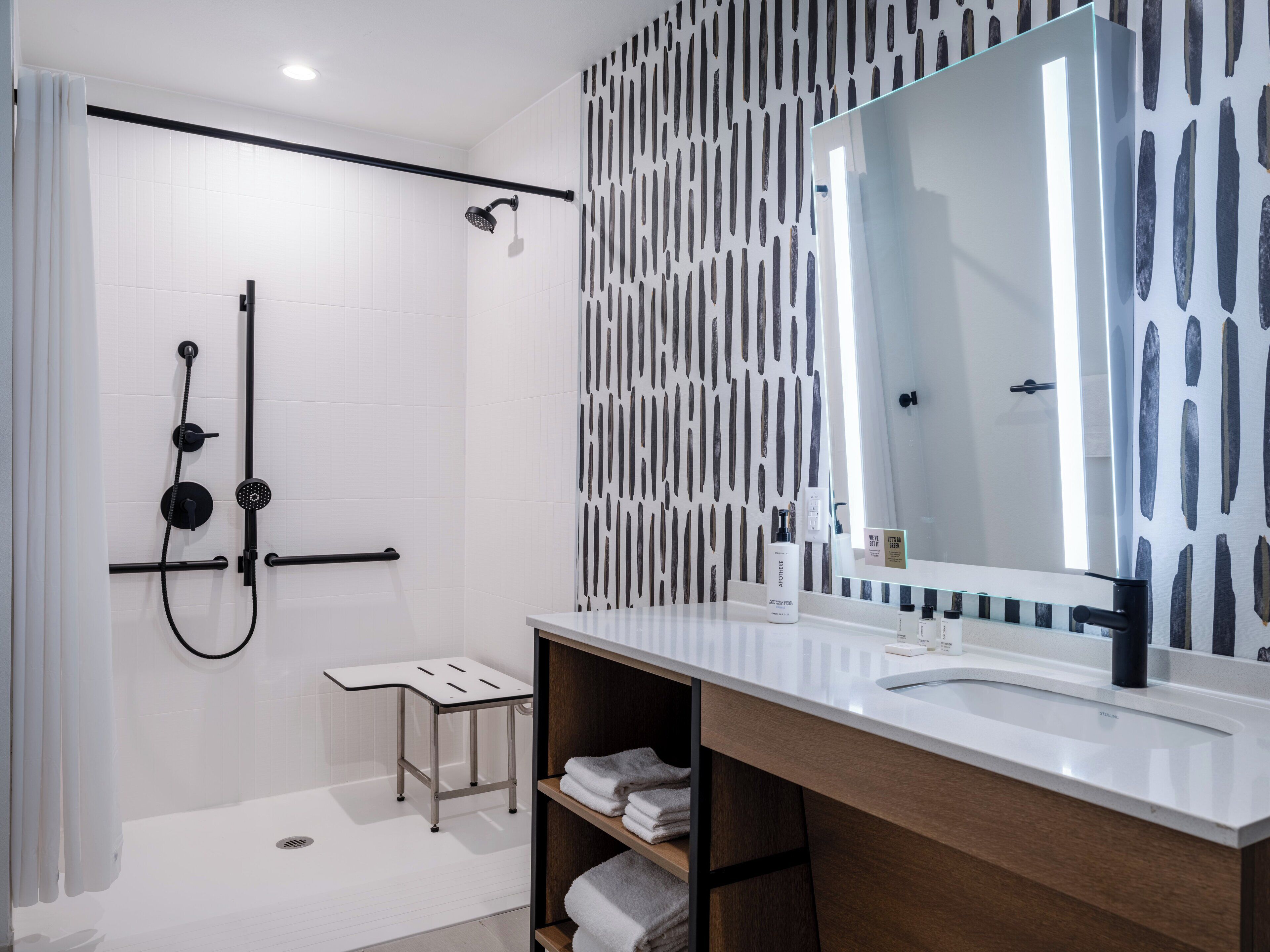 A modern bathroom with a shower, a vanity with a large mirror, and a towel rack.