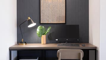 Un moderno escritorio de oficina con una computadora, teclado, ratón y una lámpara. Hay una impresora y una silla frente al escritorio.