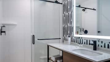Une salle de bain moderne avec une douche à parois de verre, un grand miroir et un lavabo blanc avec un meuble en bois.
