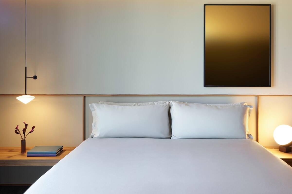 A neatly made bed with white linens, two bedside tables with lamps, and a framed picture on the wall.