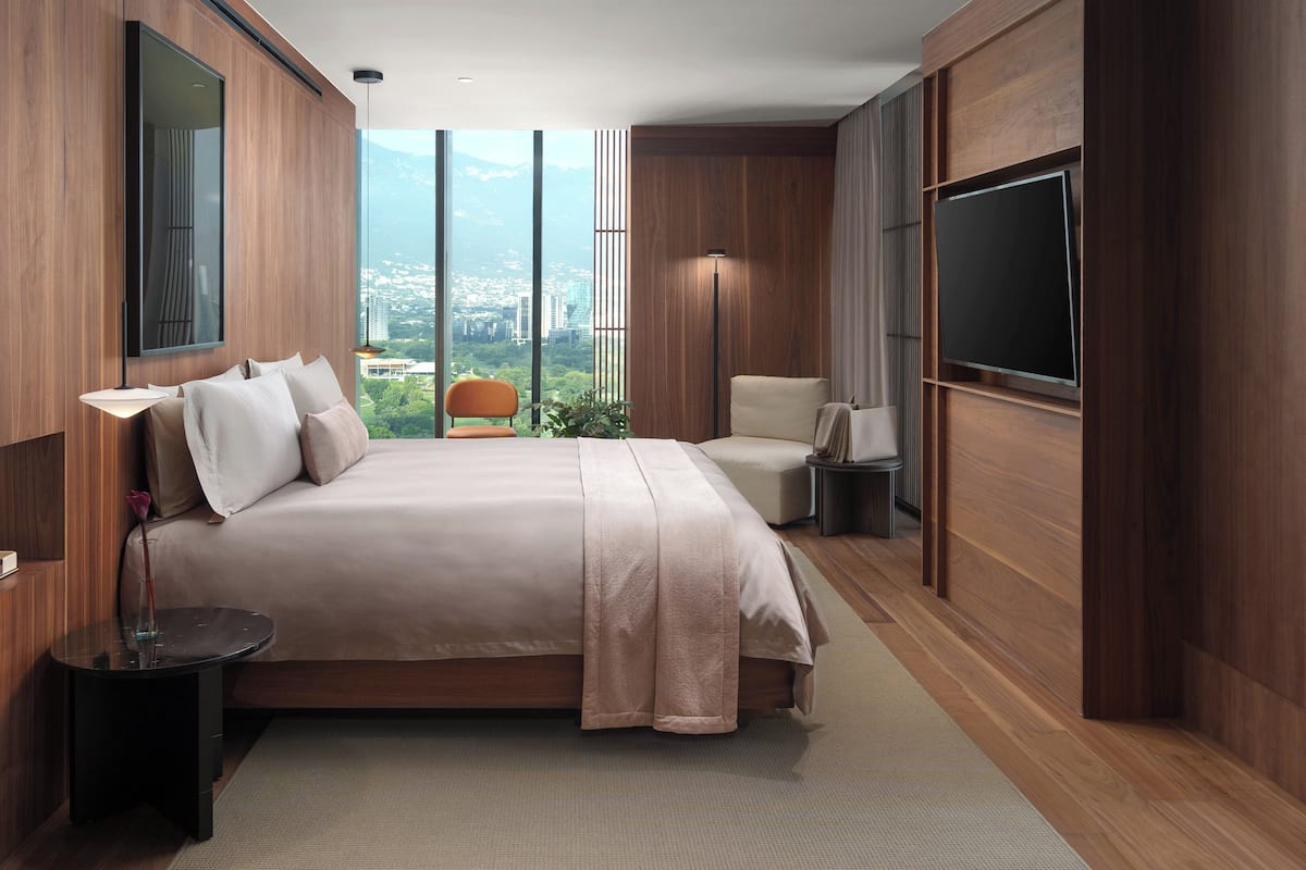 A modern bedroom with a large bed, a TV, and a city view.