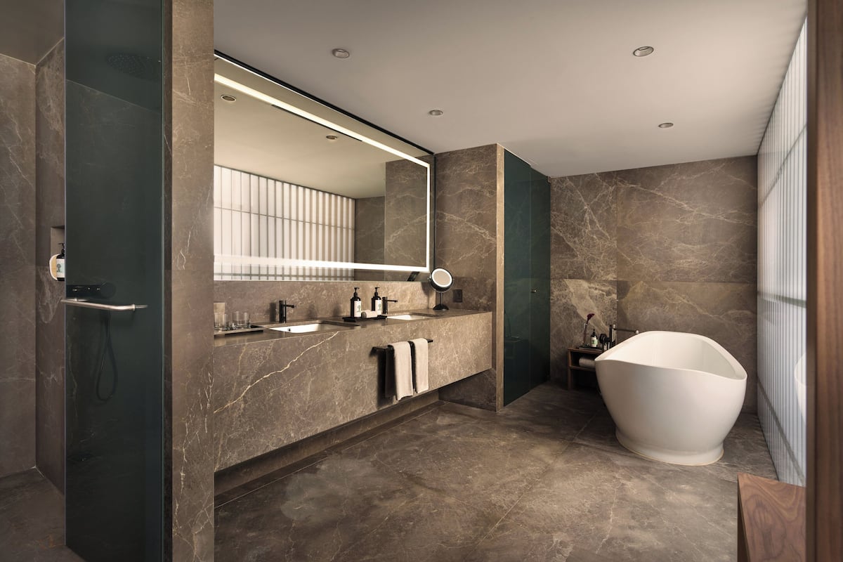 A modern bathroom with a large mirror, two sinks, a bathtub, and marble flooring.