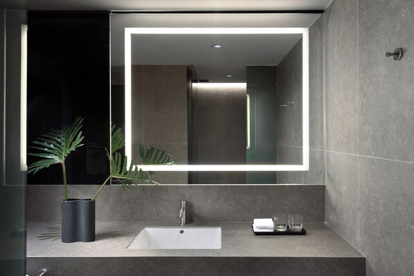 A modern bathroom with a rectangular mirror, a white sink, a potted plant, and a towel rack.