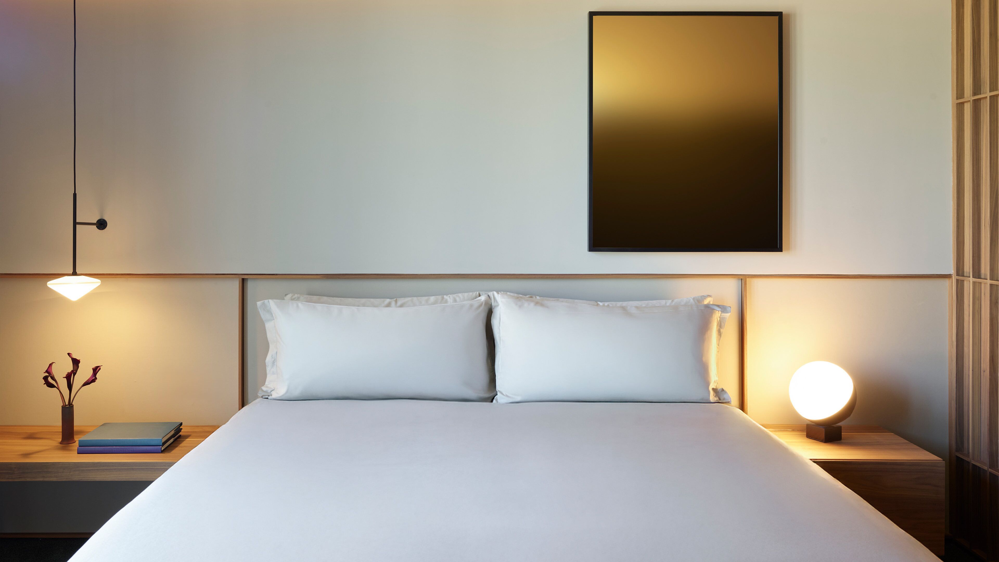 A neatly made bed with white linens, two bedside tables with lamps, and a framed picture on the wall.