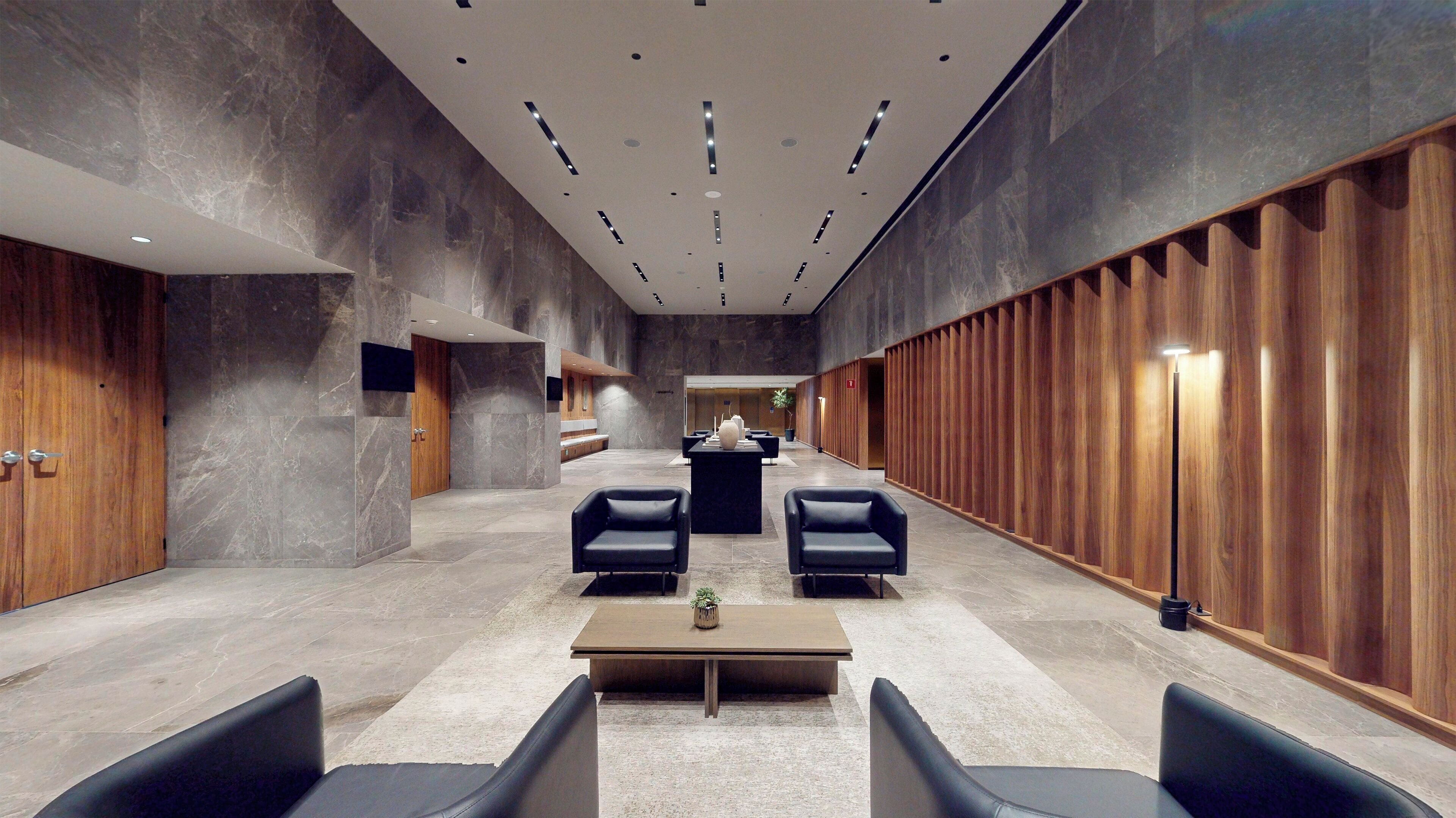 A modern lobby with a central seating area, a reception desk, and a wooden panel wall.