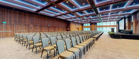 A large conference room with rows of chairs, a stage, and a wooden wall with doors.