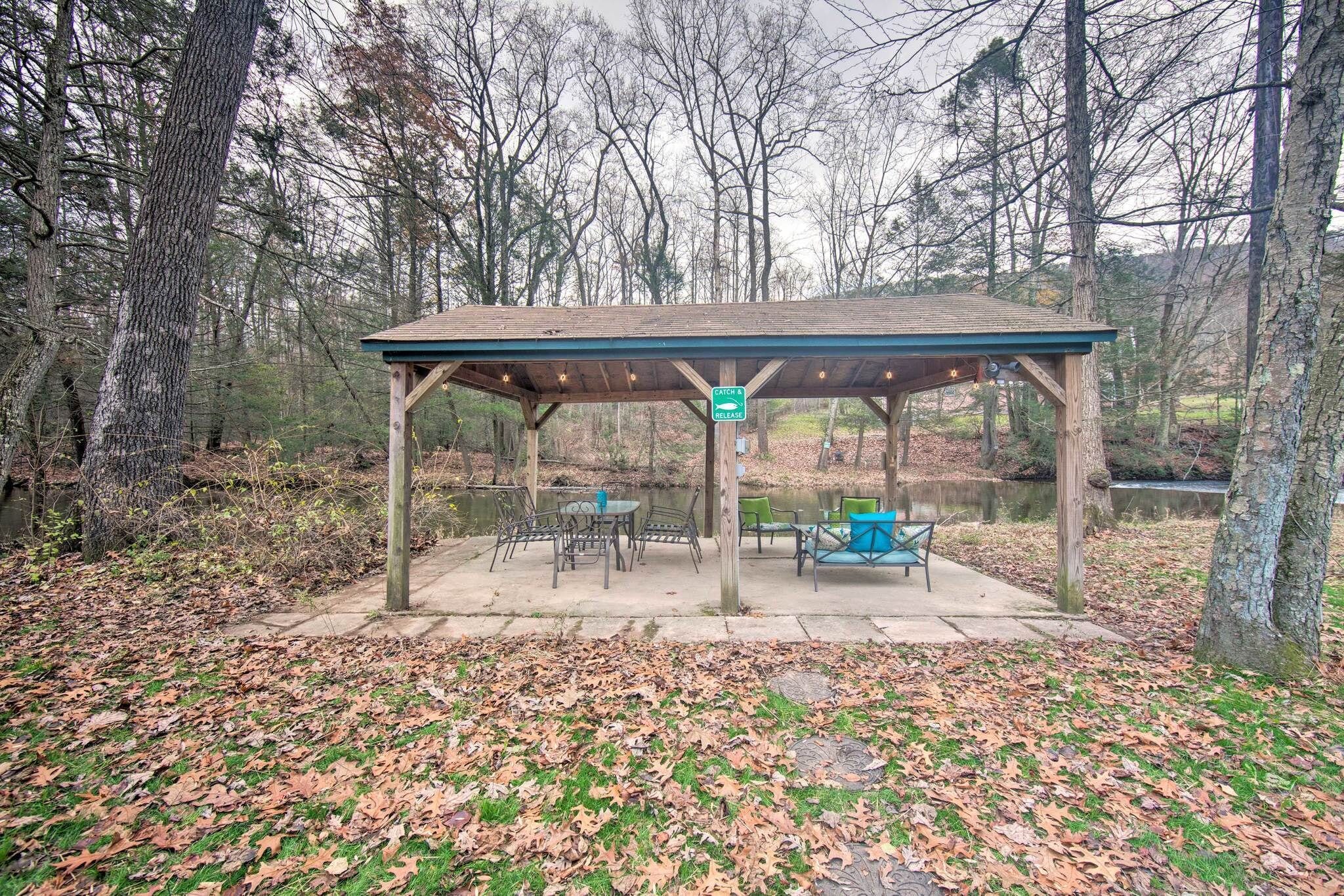 Un espace pique-nique abrité, équipé de tables et de chaises, entouré d’arbres et bordé d’un étang.