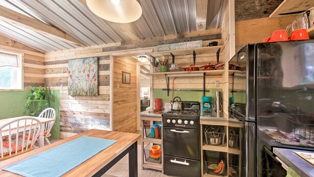 A rustic kitchen with wooden walls, a gas stove, a refrigerator, and a dining area with a table and chairs.
