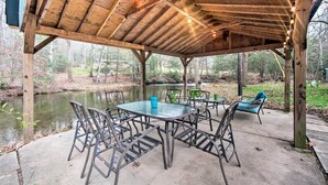 A covered outdoor seating area with a table and chairs, a wooden ceiling, and a view of a pond.