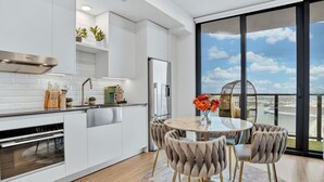 Une cuisine moderne avec des meubles blancs, une hotte en acier inoxydable et une grande fenêtre donnant sur un paysage urbain.