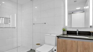 Une salle de bain moderne avec une douche à parois de verre, des toilettes blanches et un meuble-lavabo en bois avec un évier.
