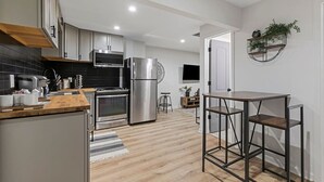 Cocina moderna con electrodomésticos de acero inoxidable, encimera de madera y un pequeño comedor con taburetes de metal.
