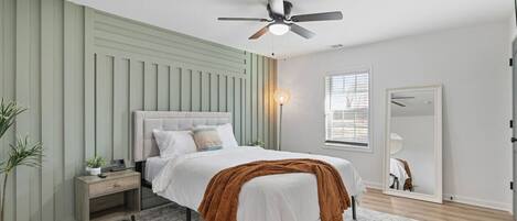 A bedroom with a bed, nightstand, bedside lamp, and a ceiling fan.