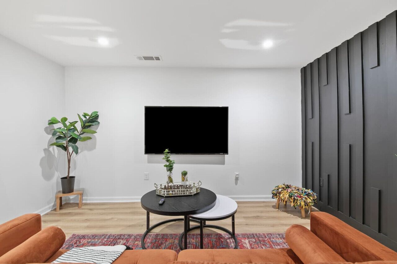 A modern living room with a flat-screen TV mounted on the wall, a round coffee table with a tray, a potted plant, and a sofa.