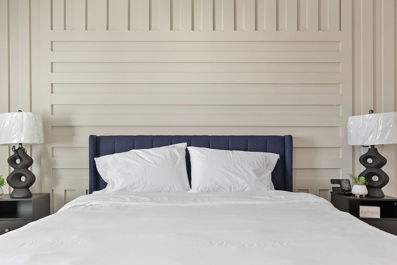 A neatly made bed with white linens, a dark blue headboard, and two bedside tables with lamps and small decorative items.