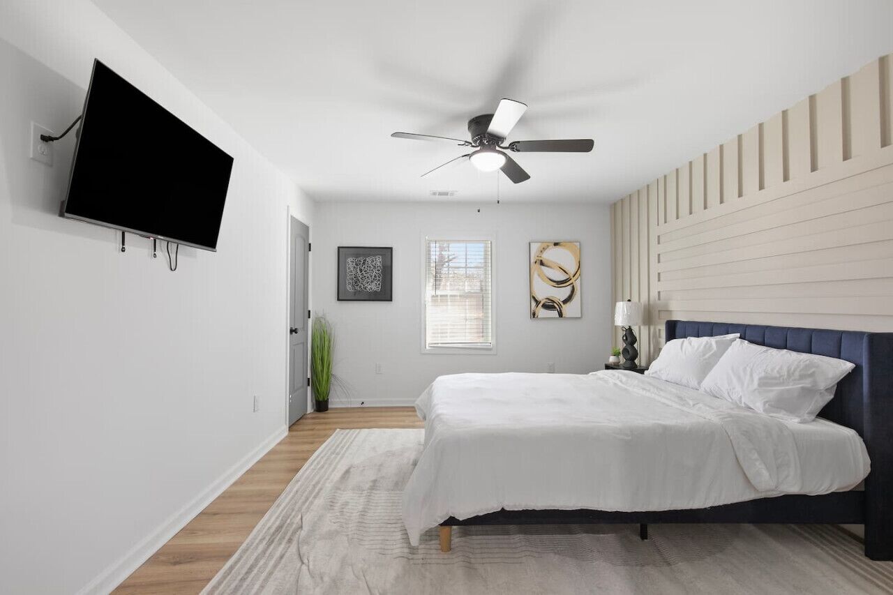 Une chambre à coucher avec un lit, un ventilateur de plafond, un téléviseur fixé au mur et des œuvres d’art accrochées au mur.