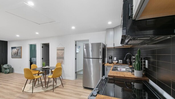 Een moderne keuken met een roestvrijstalen koelkast, een houten eettafel met gele stoelen en een zwart betegelde spatwand.