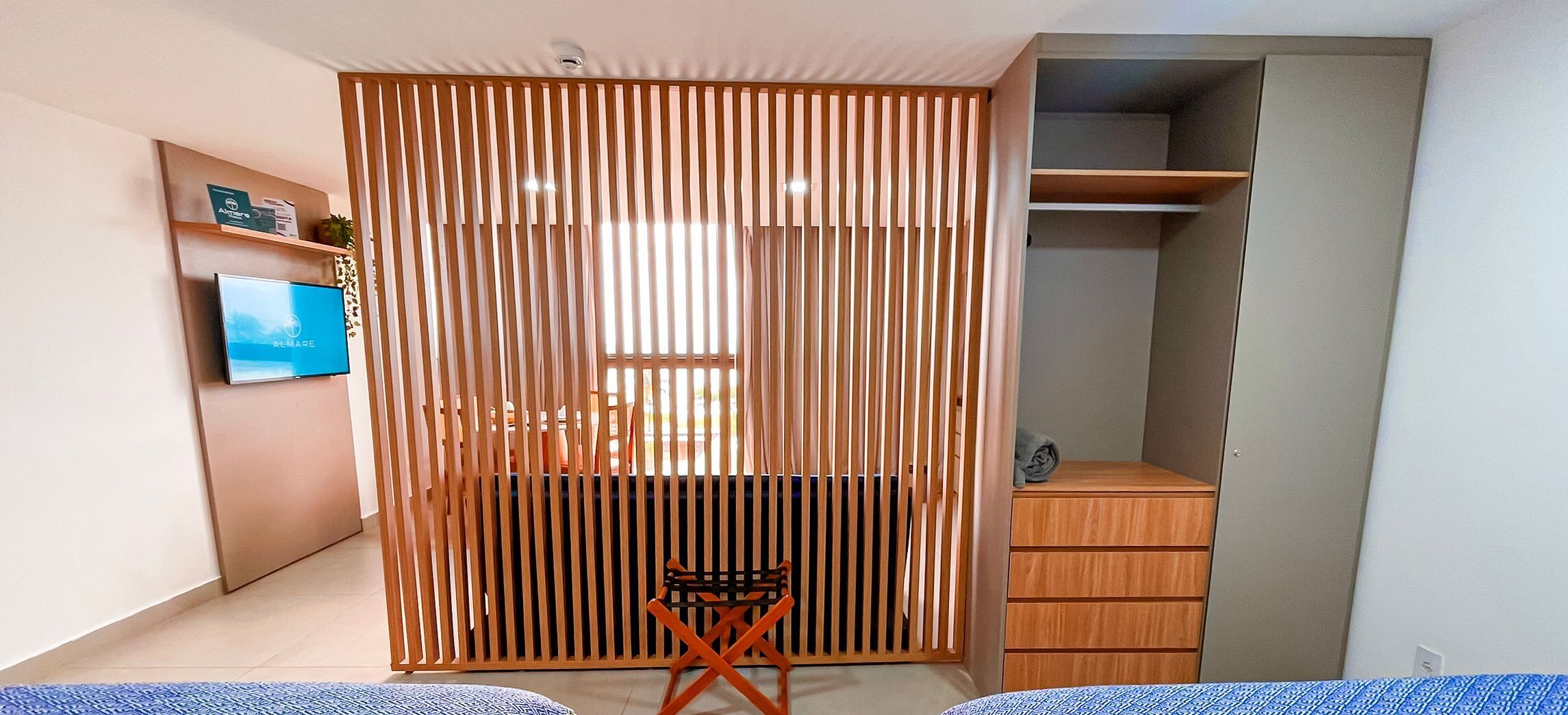 A modern bedroom with a built-in wardrobe, a small seating area, and a television on the wall.