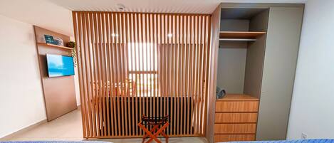 A modern bedroom with a built-in wardrobe, a small seating area, and a television on the wall.
