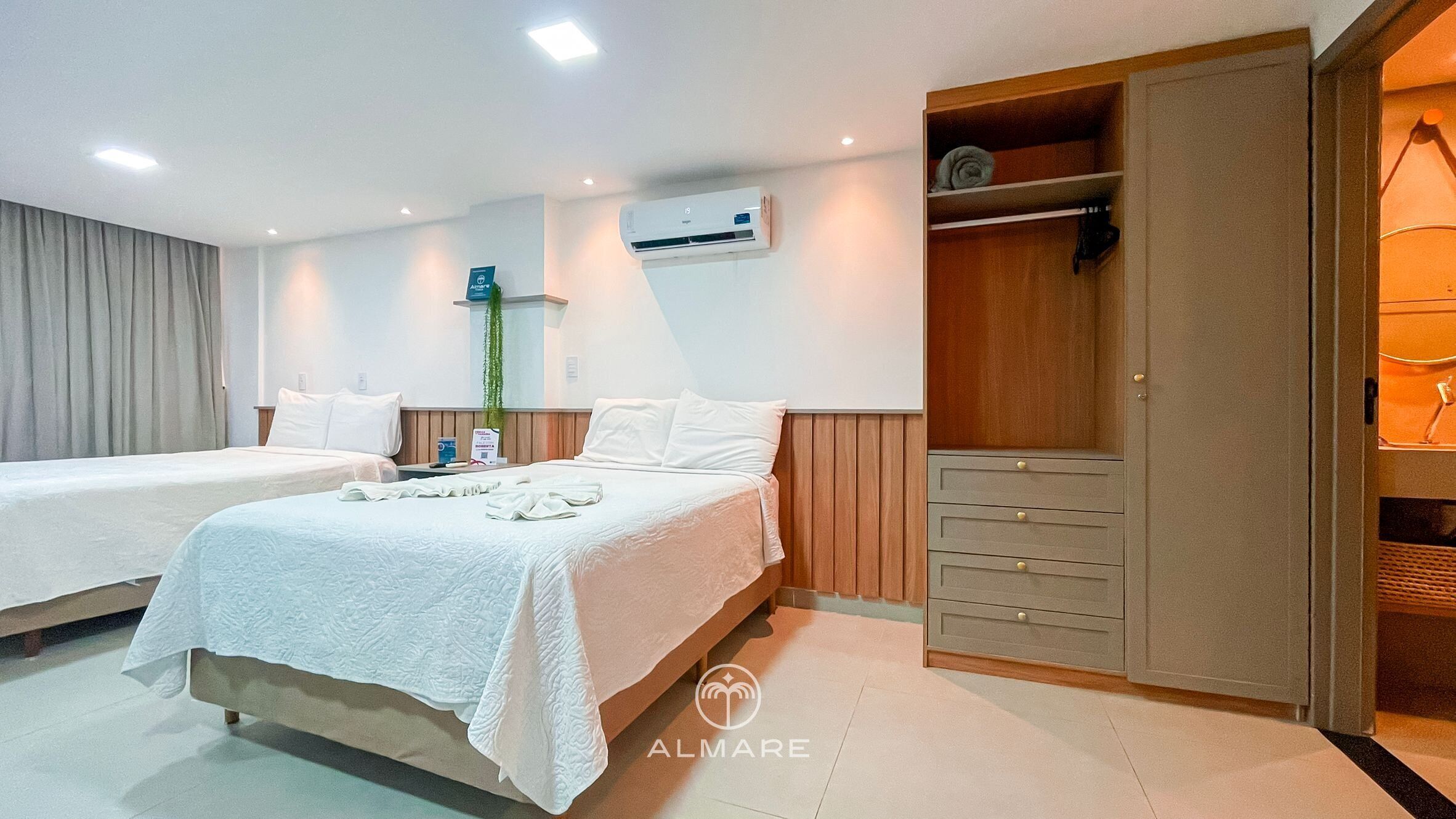 A hotel room with two beds, a wardrobe, and an air conditioning unit.