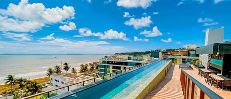 A hotel with a pool overlooking the beach, modern architecture, and a view of the ocean.