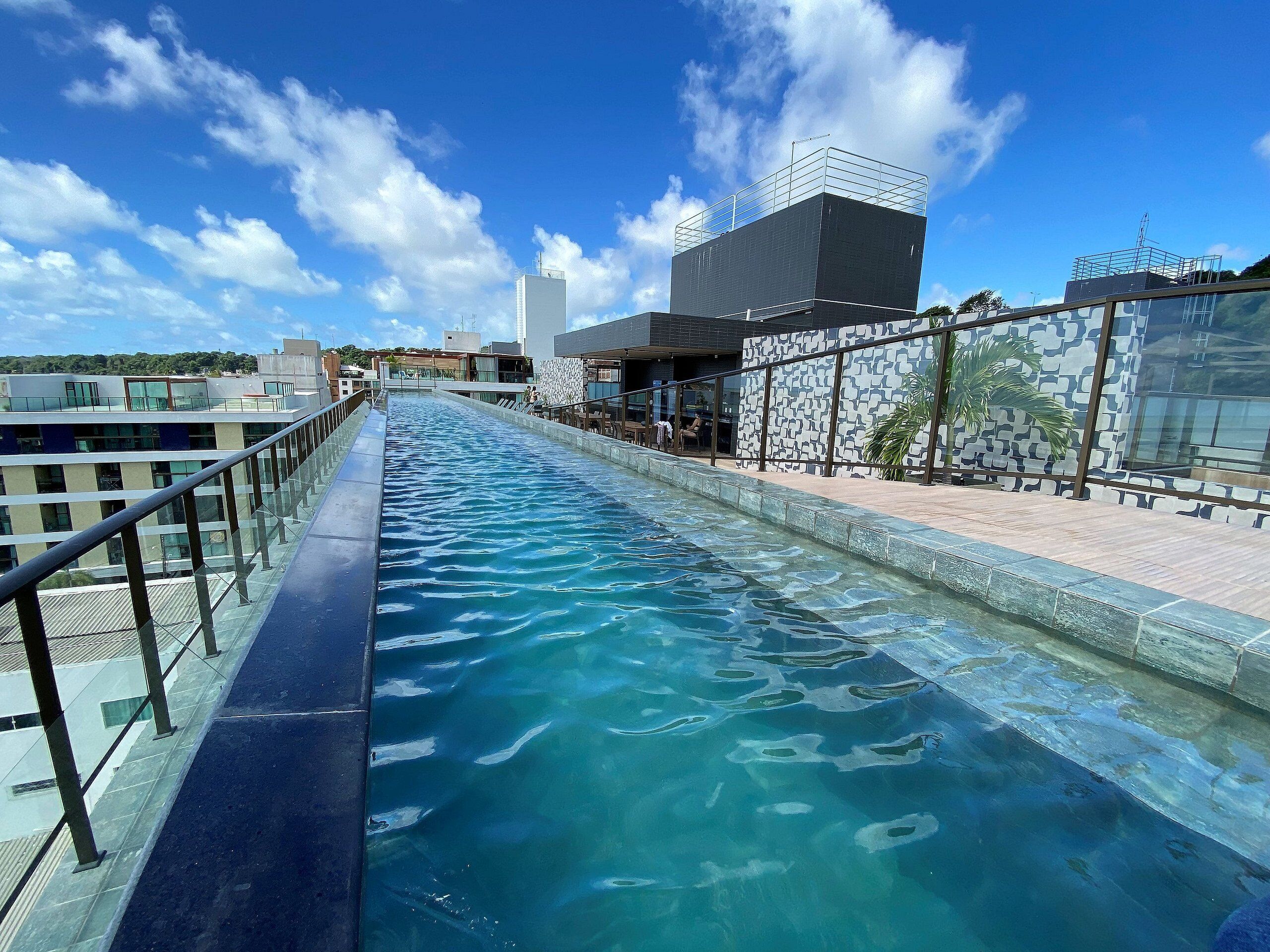 A swimming pool with a glass barrier, surrounded by modern buildings and a clear sky.