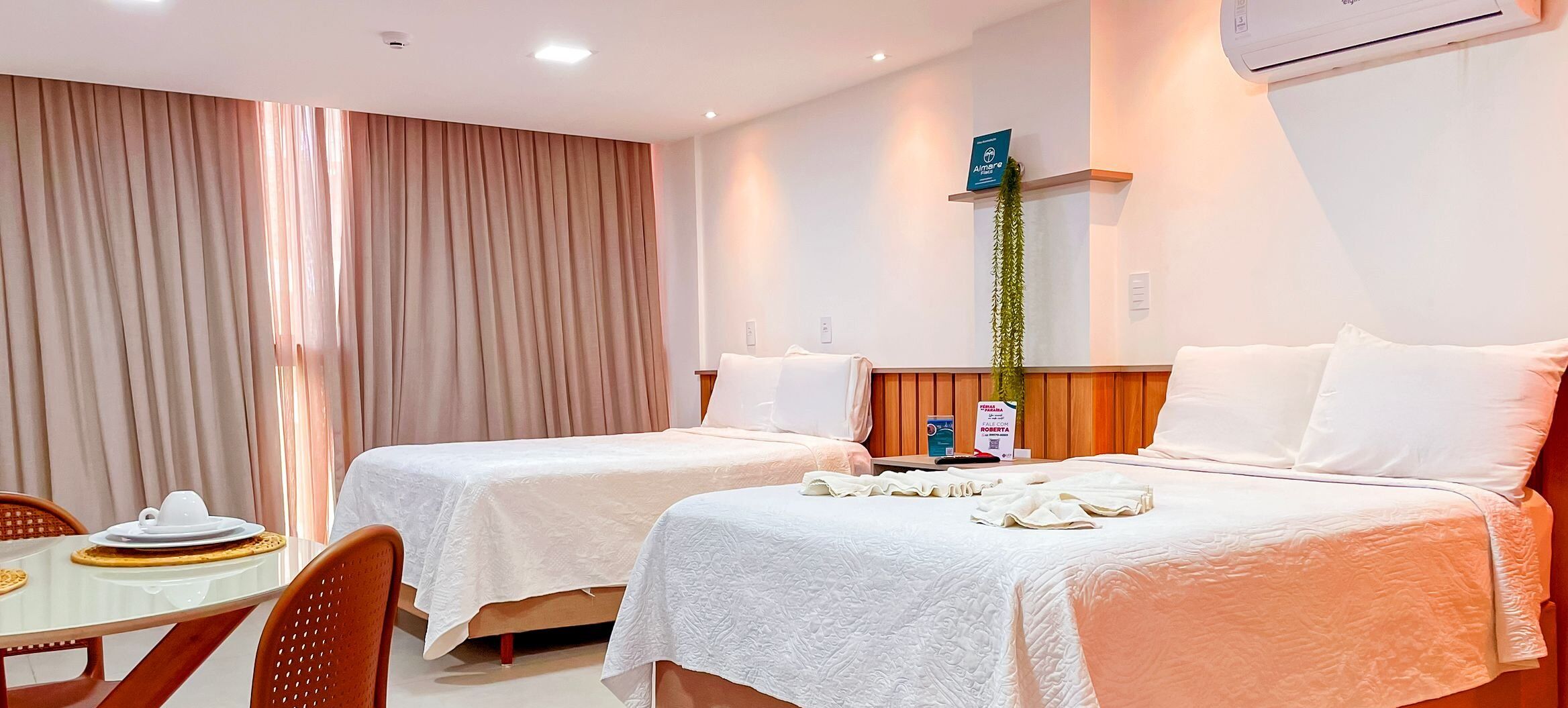 A hotel room with two beds, a dining table, and a plant.