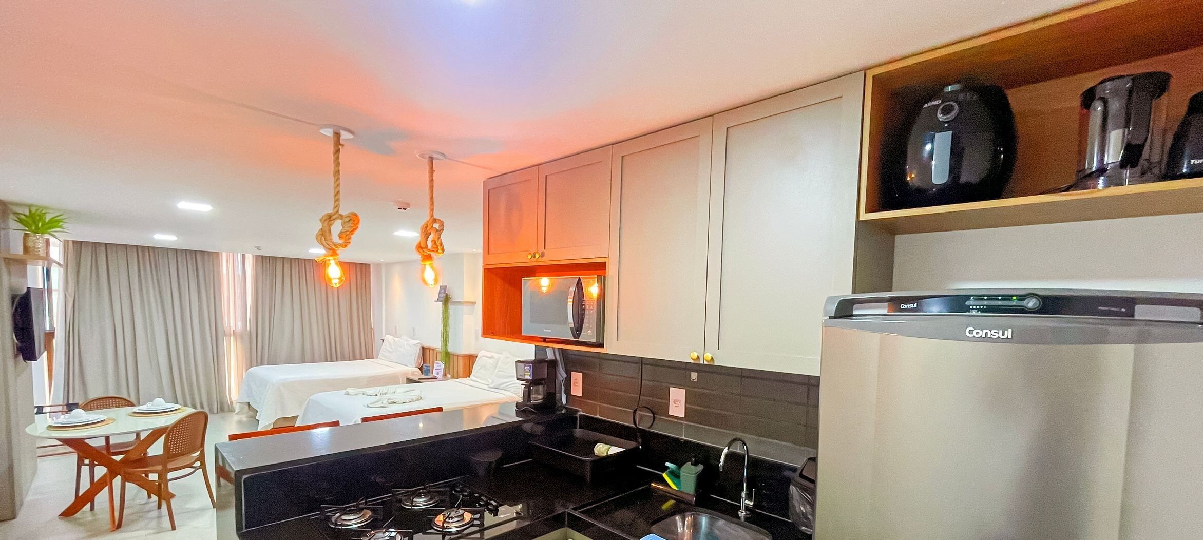 A modern hotel room with a kitchenette, a dining area, and a bed.