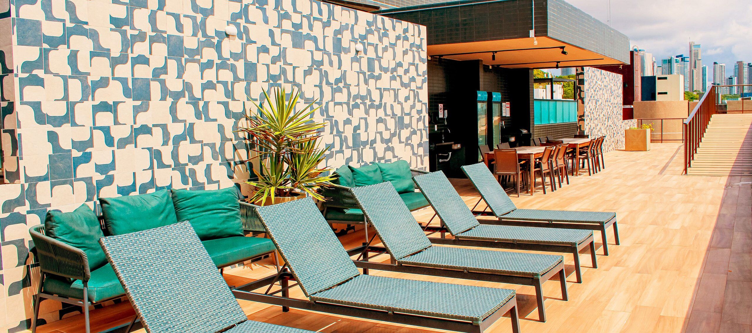 A rooftop lounge area with lounge chairs and a table, a patterned wall, and a view of the city skyline.