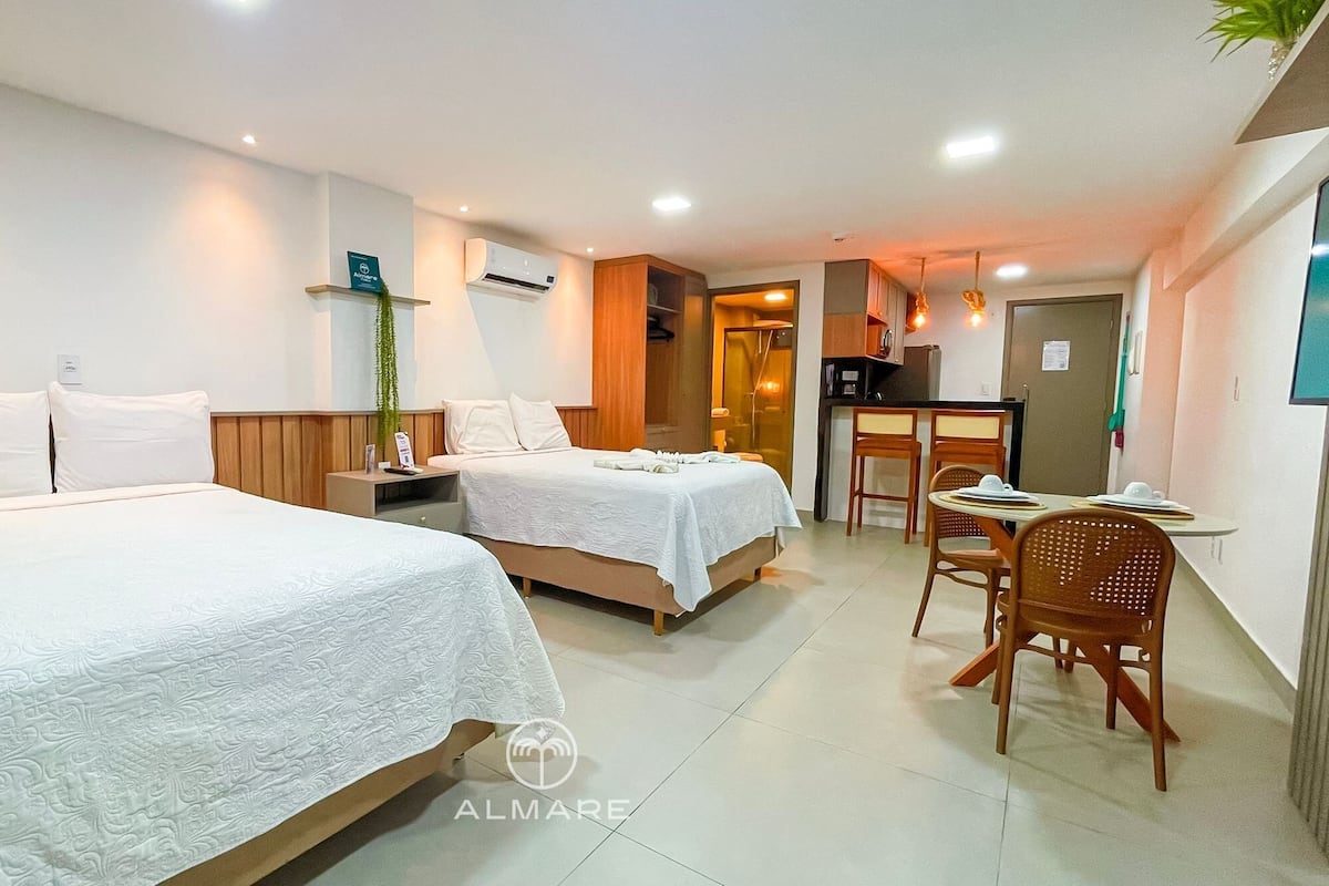 A hotel room with two beds, a small kitchenette, and a dining area.