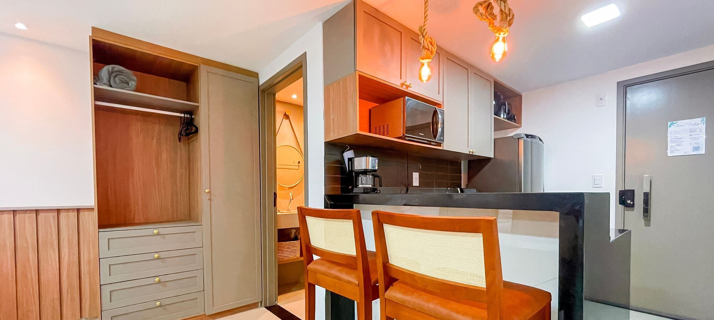Una cocina compacta con armarios de madera, un microondas, una cafetera y un refrigerador.