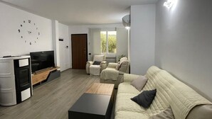 Un salon avec un canapé, des fauteuils, un téléviseur et une horloge au mur.