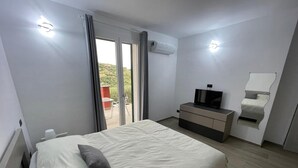 Une chambre d’hôtel équipée d’un lit, d’une télévision, d’un miroir et d’une porte-fenêtre coulissante donnant sur le balcon.