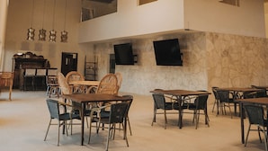 Un amplio espacio interior con techos altos, vigas a la vista y varias mesas y sillas dispuestas para comer.