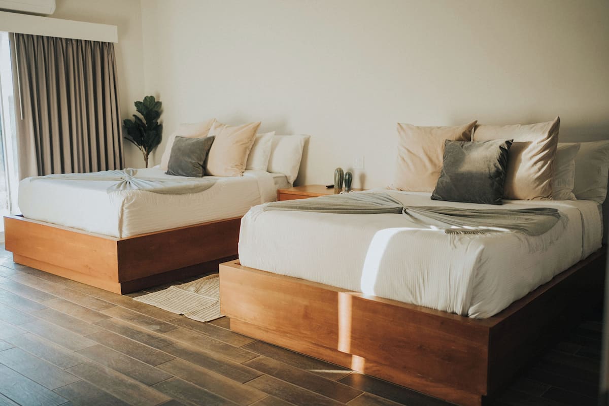 Une chambre d’hôtel moderne avec deux lits, des têtes de lit en bois et une grande fenêtre avec des rideaux.