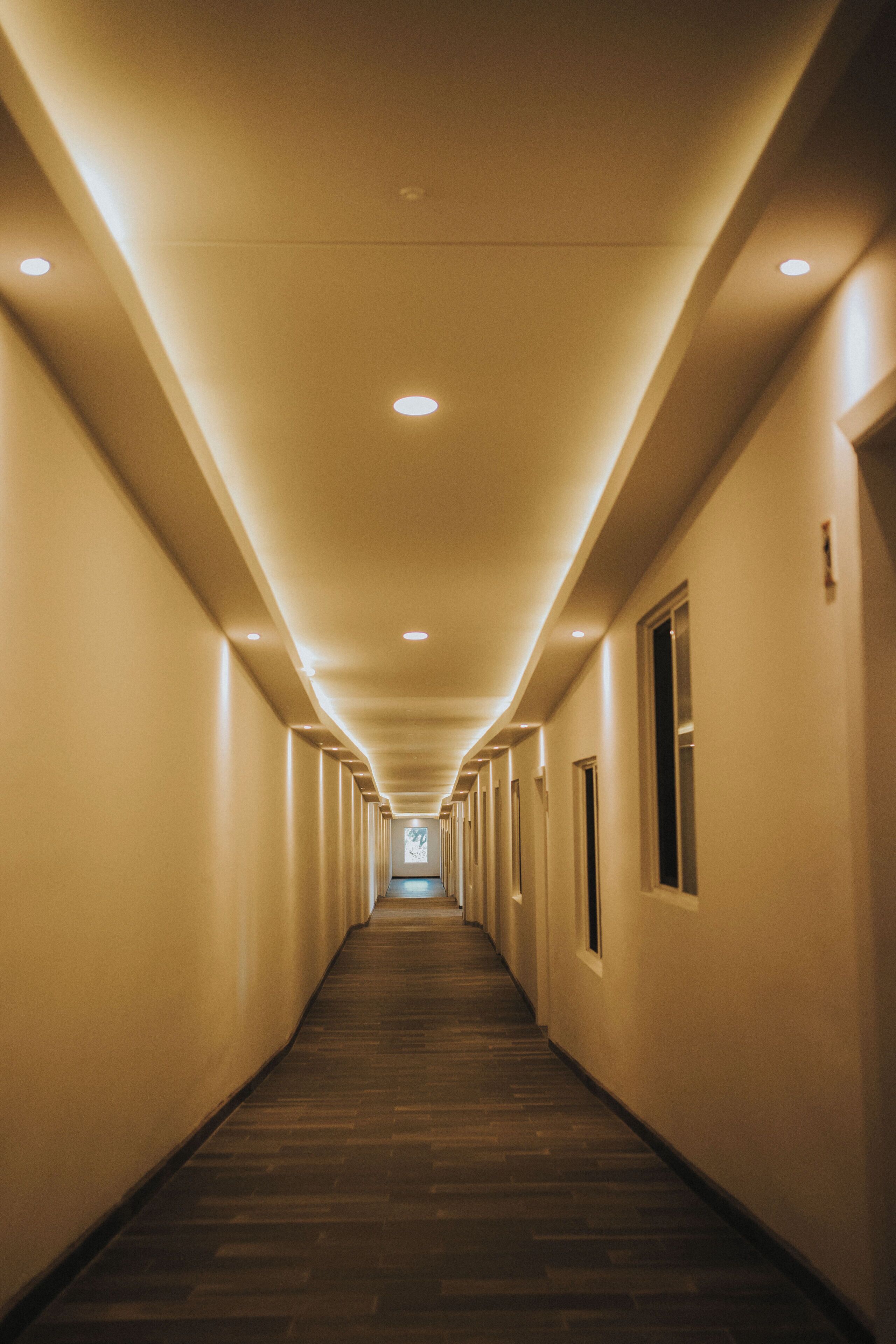 A long, narrow hotel corridor with a wooden floor and recessed lighting.
