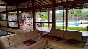 Ett rymligt inomhusområde med ett stort fönster med utsikt över en swimmingpool och en utomhusplats med sittmöbler.