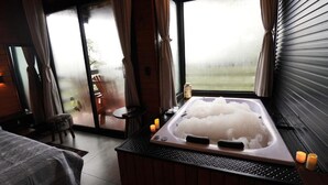 Una habitación con una bañera grande llena de agua, una cama, una mesita y vistas al exterior a través de una puerta de cristal.