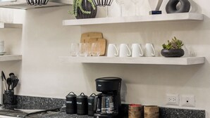 Una cocina moderna con encimera de granito, lámparas colgantes y estantes con cristalería y utensilios de cocina.