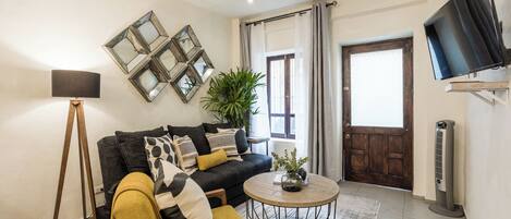 A living room with a sofa, armchairs, a coffee table, a floor lamp, a TV, and a plant.