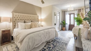 Un dormitorio con cabecera capitonada, una cama grande, ventilador de techo y vistas al exterior.