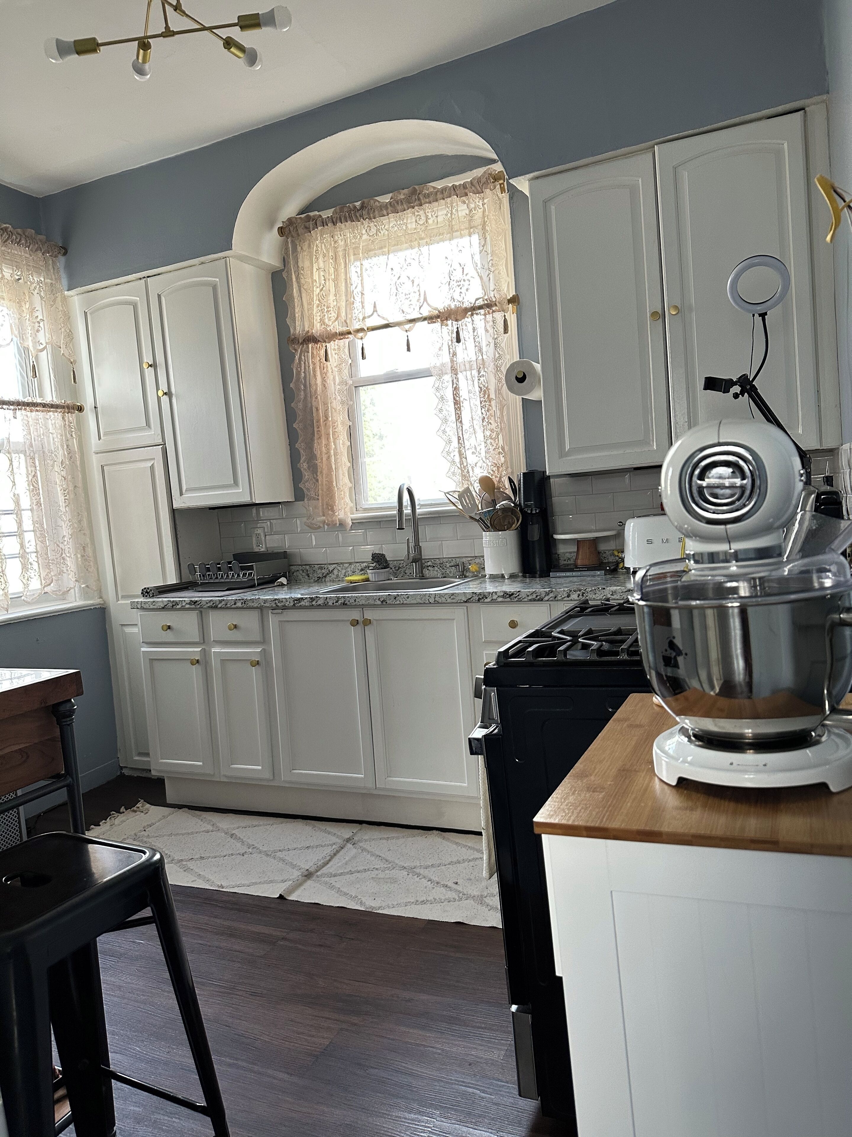 A kitchen with white cabinets, a stove, a sink, and a mixer on the counter.