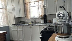 A kitchen with white cabinets, a stove, a sink, and a mixer on the counter. - ZO Family Cottage  (Mount Vernon)
