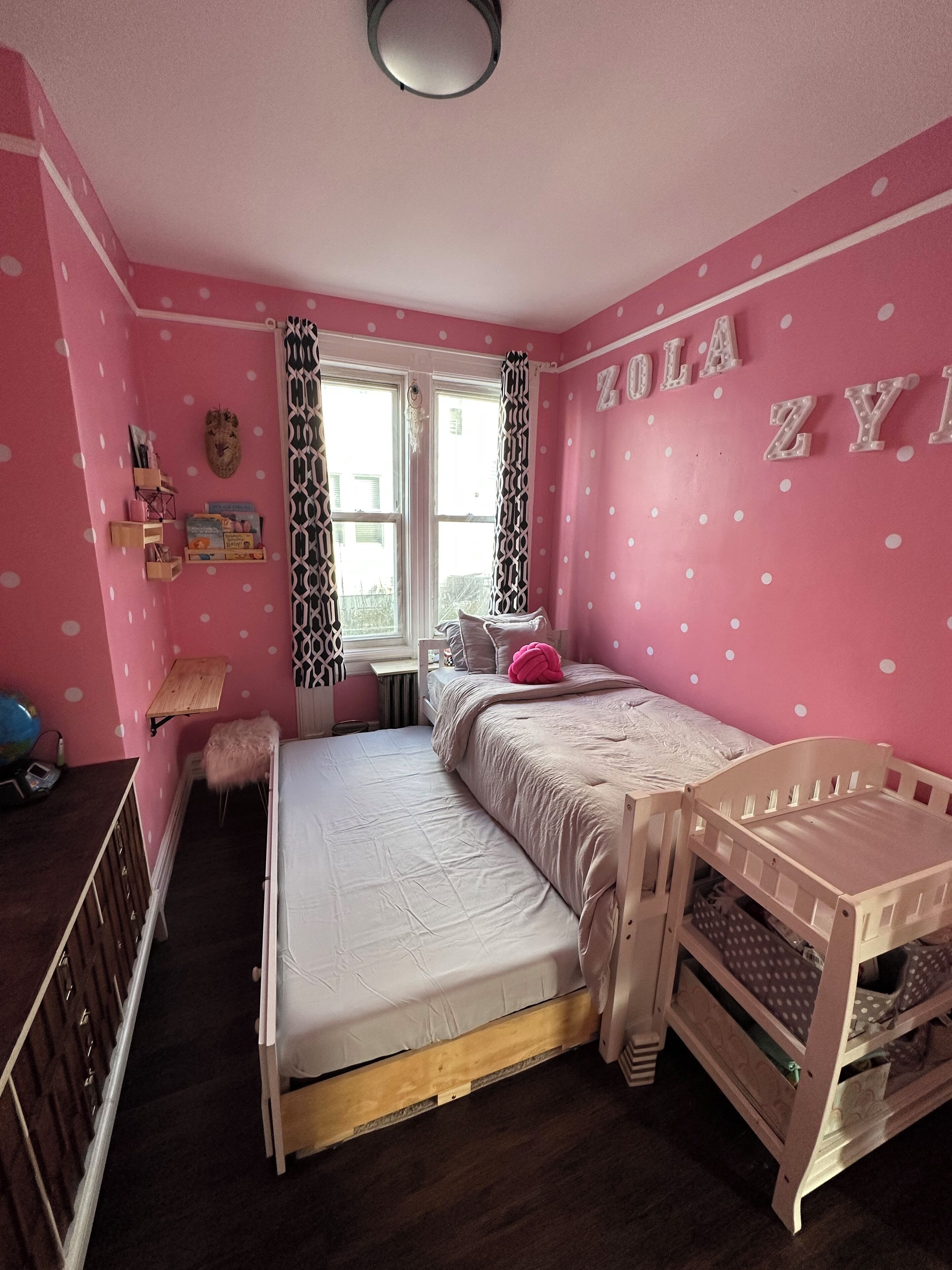 Een slaapkamer in roze tinten, met een stapelbed, een bureau en een raam met behang.