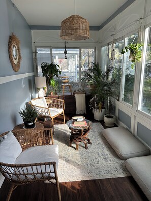A cozy room with wicker furniture, a rattan hanging light, and large windows with plants. - ZO Family Cottage (Mount Vernon)