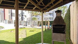 Un patio cubierto con una parrilla, suelo de baldosas y vista a un edificio residencial al fondo.